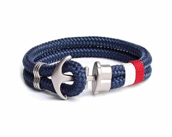 May include: A navy blue rope bracelet with a silver anchor charm and a red, white, and blue stripe.