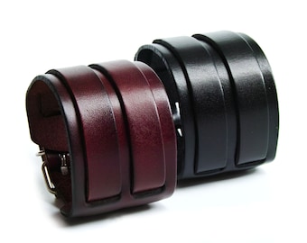 May include: Two leather bracelets, one burgundy and one black. Both bracelets have a buckle fastening and are made of multiple layers of leather.
