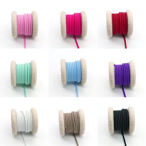 Pu&ograve; includere: Nove bobine di cordoncino elastico in vari colori, tra cui rosa, rosso, azzurro, verde menta, viola, bianco e marrone. Le bobine sono in legno e hanno una finitura naturale.