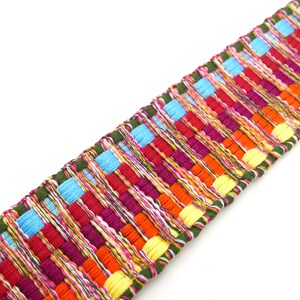 Peut inclure: Une garniture tiss&eacute;e color&eacute;e avec un motif r&eacute;p&eacute;titif de rectangles aux tons de rouge, orange, jaune, bleu et violet. La garniture a une bordure verte et convient &agrave; divers projets d'artisanat.