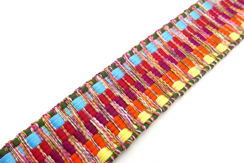 Peut inclure: Une garniture tiss&eacute;e color&eacute;e avec un motif r&eacute;p&eacute;titif de rectangles aux tons de rouge, orange, jaune, bleu et violet. La garniture a une bordure verte et convient &agrave; divers projets d'artisanat.