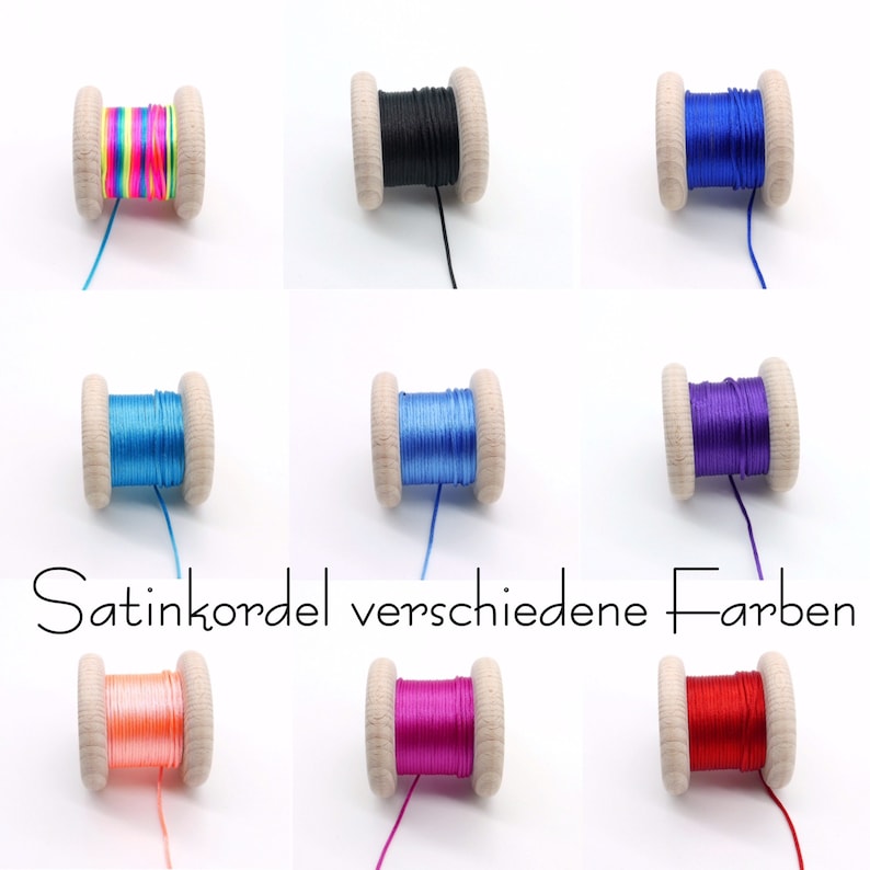 Peut inclure: Neuf bobines en bois enroul&eacute;es de cordon satin&eacute; dans diverses couleurs, notamment arc-en-ciel, noir, bleu roi, bleu clair, bleu moyen, violet, p&ecirc;che, magenta et rouge. Le texte Satinkordel verschiedene Farben est centr&eacute; sous les rang&eacute;es.