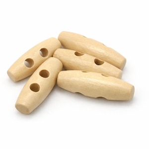 Könnte beinhalten: Eine Sammlung von fünf hellfarbigen Holzknebelknöpfen. Jeder Knopf ist länglich mit zwei Löchern zum Annähen. Die Knöpfe sind glatt und haben ein natürliches Holzmaserungs-Aussehen, geeignet für verschiedene Nähprojekte.