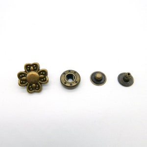 Könnte beinhalten: Vier antike goldfarbene Metallknöpfe, einer in Form einer Blume, einer mit rundem Design, einer mit runder Oberseite und einer mit spitzer Oberseite.