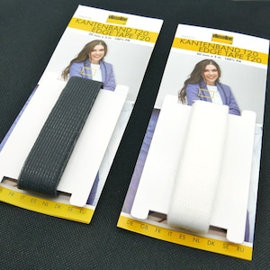 Könnte beinhalten: Zwei Packungen mit 20 mm breitem Kantenband in Weiß und Schwarz, jede Packung zeigt eine Frau im Blazer und den Text "KANTENBAND T20 EDGE TAPE T20 20 mm x 3 m 100% PA" sowie den Text "DE GB FR IT ES NL DK SE RU"