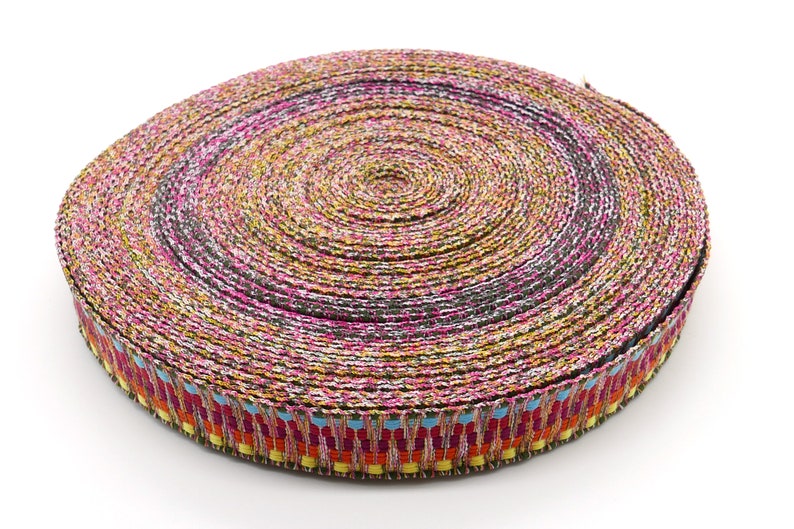 Peut inclure: Un rouleau de ruban d&eacute;coratif avec un motif tiss&eacute;. Le ruban pr&eacute;sente un m&eacute;lange de couleurs, dont le rose, le jaune, le noir et le bleu. Le bord du ruban a une bordure &agrave; motifs avec des accents rouges, oranges, jaunes et bleus.