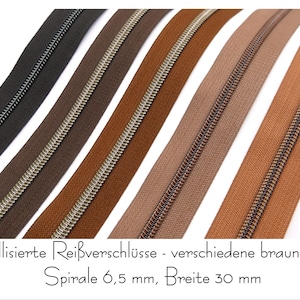Könnte beinhalten: Fünf verschiedene braune Reißverschlussbänder mit silbernen Metallzähnen. Die Reißverschlussbänder sind in einer Reihe angeordnet, wobei das dunkelste braune Band oben und das hellste braune Band unten liegt. Der Text "metallisierte Reißverschlüsse - verschiedene braun Töne Spirale 6,5 mm, Breite 30 mm" ist am unteren Rand des Bildes sichtbar.