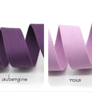 May include: Two rolls of woven cotton webbing, one in aubergine and one in pink. The webbing is a textured, flat, and narrow strip of fabric.
