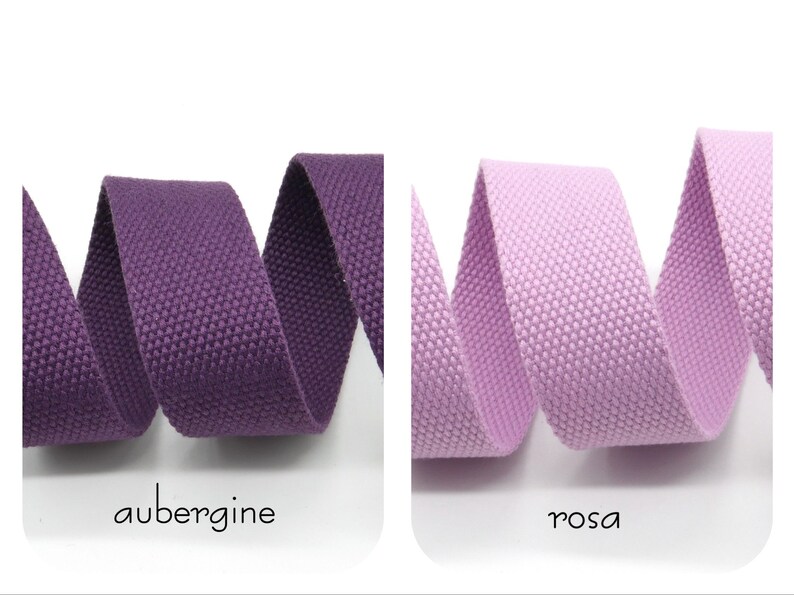 May include: Two rolls of woven cotton webbing, one in aubergine and one in pink. The webbing is a textured, flat, and narrow strip of fabric.