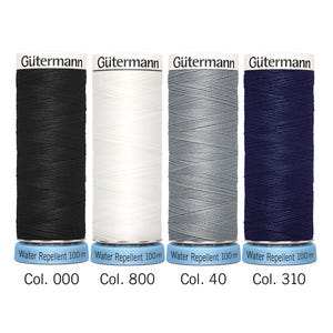 Puede incluir: Cuatro carretes de hilo Gütermann en negro, blanco, gris y azul marino. Cada carrete está etiquetado con el código de color y el texto "Water Repellent 100m". El hilo está enrollado en una base de plástico azul.