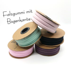 Può includere: Quattro bobine di passamaneria in tessuto con bordi a festoni. La passamaneria è rosa, nera, viola e verde chiaro. Le bobine sono impilate l'una sull'altra. Il testo "Falzgummi mit Bogenkante" è visibile nell'immagine.