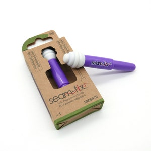 Könnte beinhalten: Ein lila Nahttrenner mit weißer Spitze und dem Text "seam-fix" wird neben seiner Kartonverpackung angezeigt. Die Verpackung trägt den Text "Mini Nahttrenner" in mehreren Sprachen. Das Produkt ist zum Nähen und Basteln bestimmt.