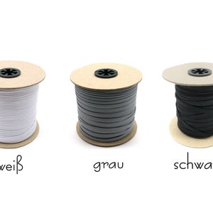 May include: Three spools of elastic cord, one white, one gray, and one black, each wound around a cardboard spool with a label underneath. The labels read "wei&szlig;", "grau", and "schwarz".