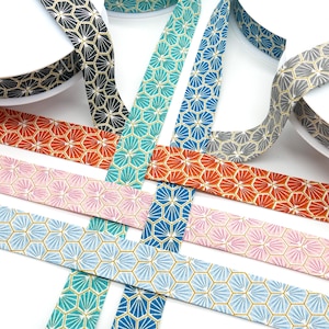 May include: A selection of patterned ribbons in shades of black, teal, orange, pink, grey, and blue. Each ribbon displays a repeating geometric design with gold detailing. The ribbons are unrolled and presented against a white backdrop.
