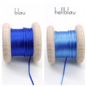 Peut inclure: Deux bobines en bois enroul&eacute;es de cordon. La bobine de gauche pr&eacute;sente un cordon bleu fonc&eacute; avec l'inscription 'blau', et celle de droite un cordon bleu clair avec l'inscription 'hellblau'. Les bobines ont une finition en bois naturel.