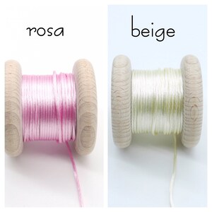 Peut inclure: Deux bobines en bois enroul&eacute;es de cordon fin. La bobine de gauche est &eacute;tiquet&eacute;e 'rosa' et contient du cordon rose clair. La bobine de droite est &eacute;tiquet&eacute;e 'beige' et contient du cordon beige p&acirc;le. Les deux bobines ont un fini en bois naturel.