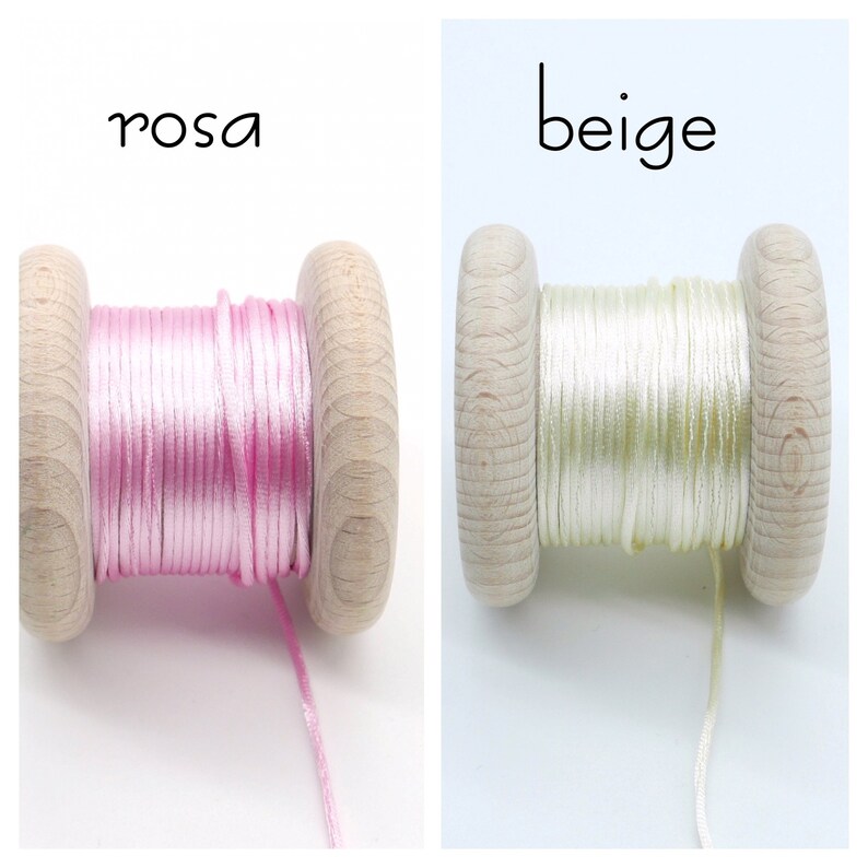 Peut inclure: Deux bobines en bois enroul&eacute;es de cordon fin. La bobine de gauche est &eacute;tiquet&eacute;e 'rosa' et contient du cordon rose clair. La bobine de droite est &eacute;tiquet&eacute;e 'beige' et contient du cordon beige p&acirc;le. Les deux bobines ont un fini en bois naturel.