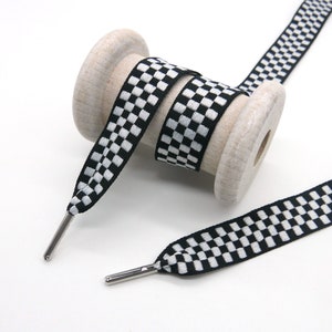 May include: Black and white checkered ribbon wound around a wooden spool. The ribbon has silver metal tips.