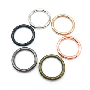 May include: Six metal rings in different finishes: silver, gold, black, gunmetal, copper, and rose gold. The rings are all the same size and are arranged in a circle.