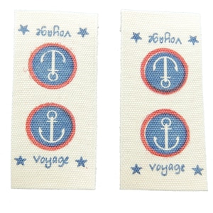 May include: Two white fabric labels with red and blue anchor designs. The labels have the text "voyage" and "bonjour" printed on them.