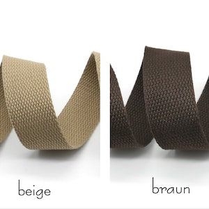 May include: Two rolls of woven cotton webbing, one beige and one brown. The webbing is textured and has a subtle sheen.