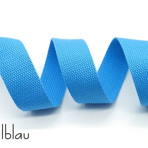 May include: A close-up of a light blue woven cotton webbing ribbon. The ribbon is coiled and the texture of the fabric is visible.