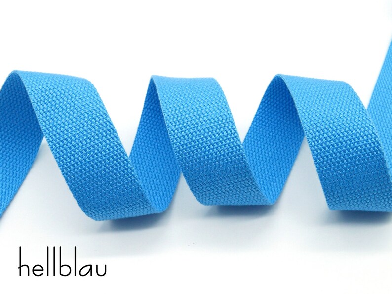 May include: A close-up of a light blue woven cotton webbing ribbon. The ribbon is coiled and the texture of the fabric is visible.