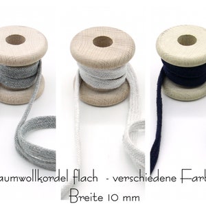 Könnte beinhalten: Drei Spulen flaches Baumwollkordel in Grau, Weiß und Dunkelblau. Jede Spule ist 10 mm breit. Der Text "Baumwollkordel flach - verschiedene Farben" und "Breite 10 mm" ist unter den Spulen sichtbar.