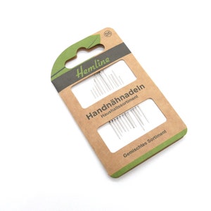 Könnte beinhalten: Eine Packung mit verschiedenen Handnähnadeln von Hemline. Die Verpackung ist braun mit grünen Akzenten und trägt die Aufschrift "Handnähnadeln Haushalts Sortiment" und "Gemischtes Sortiment".