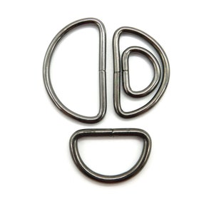 Könnte beinhalten: Satz mit vier schwarzen D-Ringen aus Metall in verschiedenen Größen. Die Ringe sind glatt und haben eine polierte Oberfläche.