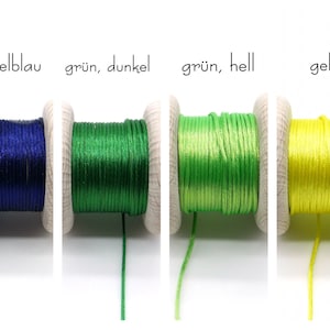 Peut inclure: Quatre bobines en bois enroul&eacute;es de cordon satin&eacute; brillant en bleu fonc&eacute;, vert fonc&eacute;, vert clair et jaune. Le texte au-dessus des bobines indique dunkelblau, gr&uuml;n, dunkel, gr&uuml;n, hell et gelb, pr&eacute;cisant la couleur de chaque cordon.