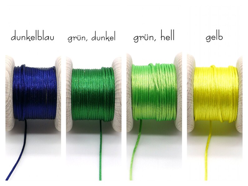 Peut inclure: Quatre bobines en bois enroul&eacute;es de cordon satin&eacute; brillant en bleu fonc&eacute;, vert fonc&eacute;, vert clair et jaune. Le texte au-dessus des bobines indique dunkelblau, gr&uuml;n, dunkel, gr&uuml;n, hell et gelb, pr&eacute;cisant la couleur de chaque cordon.