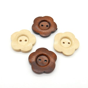 May include: Four flower-shaped wooden buttons in varying shades of brown and beige. Each button has two small holes for sewing. The buttons are arranged on a white background, showcasing their natural wood grain and floral design.