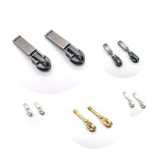 May include: A selection of metal zipper pulls in different styles and finishes. The image displays several pairs of pulls in silver, gunmetal, and gold tones. The designs include rectangular and decorative shapes, suitable for clothing and craft projects.