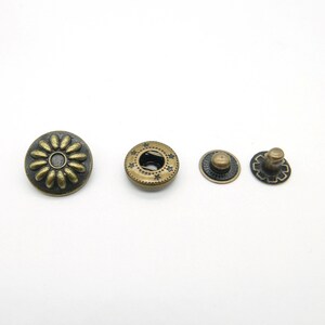 Op de afbeelding: Vier antieke goudkleurige metalen drukknopen. Eén drukknoop heeft een decoratief bloemmotief, een andere heeft een stermotief en de andere twee zijn simpel.