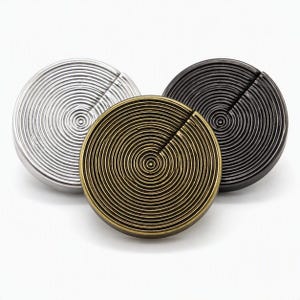 Pode incluir: Três puxadores circulares com um padrão de anéis concêntricos que irradiam a partir do centro. Cada puxador tem uma única ranhura reta que se estende do centro até à extremidade exterior. O conjunto inclui um acabamento prateado, latão e preto.