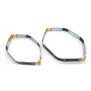 Può includere: Due cerchi in metallo nero con cerniere dorate. I cerchi sono collegati da una serie di piccoli rivetti in metallo. Il cerchio più grande ha un diametro di circa 25 cm, e il più piccolo di circa 18 cm.