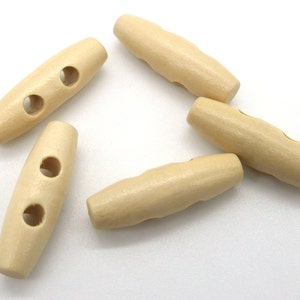 Może przedstawiać: Kolekcja pięciu jasnobeżowych drewnianych guzików typu toggle. Każdy guzik jest podłużny z zaokrąglonymi końcami i dwoma otworami do szycia. Guziki są gładkie i mają naturalny wygląd słojów drewna.