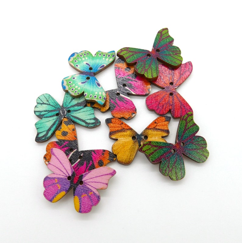 May include: Assortment of colorful wooden butterfly buttons with painted designs. The buttons are in various shades of green, blue, pink, orange, and yellow.