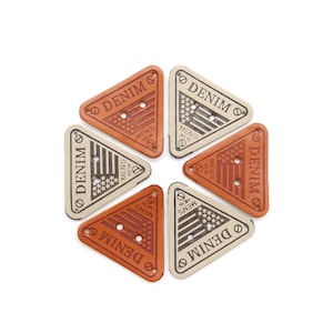 Könnte beinhalten: Sechs dreieckige Stoff-Patches mit dem Wort "DENIM" in einem Kreis um ein kleines amerikanisches Flaggen-Design gedruckt. Die Patches sind in zwei Farben: Braun und Beige.
