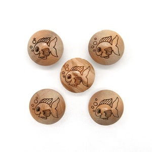 Op de afbeelding: Vijf houten knopen met een bruine houtnerf. Elke knop heeft een cartoonvis met bubbels, omlijnd in zwart.