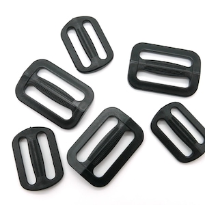 May include: Six black plastic slider buckles, each with a rectangular shape and a center bar for sliding through straps or webbing.
