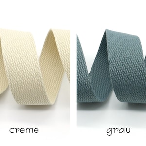 May include: Two rolls of woven cotton webbing, one in cream and one in gray. The webbing is textured and has a subtle sheen.