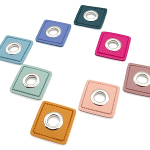 Può includere: Assortimento di otto occhielli in pelle di forma quadrata in vari colori, tra cui turchese, rosa, blu, verde e marrone. Ogni occhiello ha un anello di metallo argentato al centro.