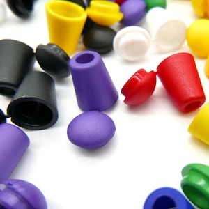Pode incluir: Conjunto de pontas de cordão de plástico coloridas em vários formatos e tamanhos. As pontas de cordão são de cor roxa, vermelha, amarela, preta e verde.