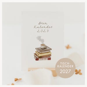 Puede incluir: Un calendario de escritorio blanco con el texto "Dein Kalender 2027" y una ilustración en acuarela de una pila de libros coronada por una taza de café humeante. Una insignia circular beige muestra el texto "TISCH-KALENDER 2027" en letras blancas.