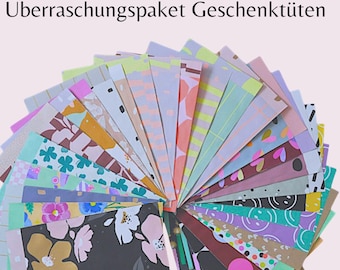 Puede incluir: Un abanico de bolsas de regalo con patrones coloridos en varios diseños, incluyendo patrones florales, geométricos y abstractos. El texto "Überraschungspaket Geschenktueten" es visible en la parte superior de la imagen.