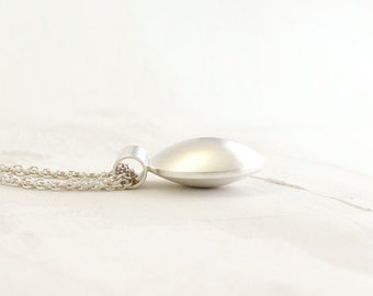 Puede incluir: Un collar de plata con un colgante redondo y ligeramente abovedado. La cadena es de estilo delicado y de eslabones.