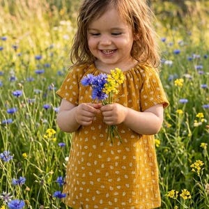 Könnte beinhalten: Ein senfgelbes kurzärmeliges Kleid mit kleinem weißem Blumenmuster, gerafftem Rundhalsausschnitt und lockerer Passform, getragen beim Halten eines kleinen Straußes aus blauen Kornblumen und gelben Wildblumen auf einem Feld.