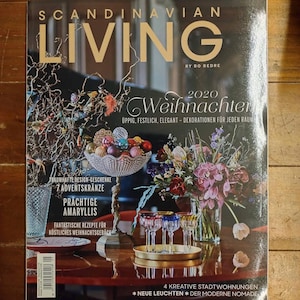 May include: Scandinavian Living magazine cover featuring a 2020 Christmas theme. The cover features a festive arrangement of ornaments, flowers, and glassware on a wooden table. The magazine title is in gold lettering and the text "Weihnachten" is in a decorative script font.